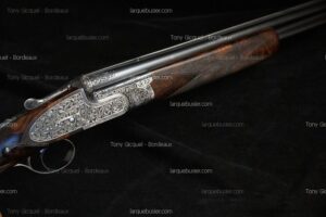 Fusil de chasse luxueux avec bascule finement gravée de motifs floraux, crosse et devant en bois sombre. Canons superposés brillants.