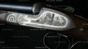 Fusil de chasse finement gravé : scène détaillée avec chien de chasse et oiseau en vol, entourée d'ornements. Texte visible "Tony Gicquel - Bordeaux" et "larquebusier.com".