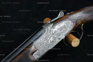 Fusil de chasse luxueux avec bascule argentée richement gravée de scènes de chasse et rinceaux. Crosse en bois veiné. Marque Tony Gicquel - Bordeaux, larquebusier.com.