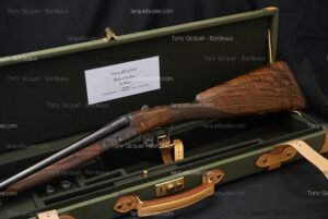 Fusil de chasse juxtaposé dans son étui vert doublé de cuir. La crosse en bois veiné repose sur le velours. Carte "Tony Gicquel - Fusils & Carabines De Chasse" visible.