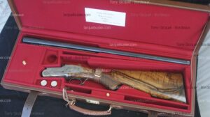 Fusil de chasse Tony Gicquel démonté dans sa mallette rouge. Le bois de la crosse est veiné, l'action gravée. La carte indique 'Armes et Canons de Chasse, Bordeaux'.