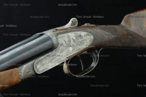 Fusil de chasse en bois et métal gravé, montrant des gravures fines d'oiseaux sur la platine. Texte visible: Tony Gicquel - Bordeaux, larquebusier.com.