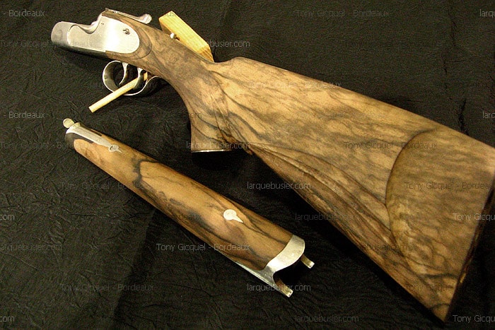 Fusil démonté en gros plan : crosse et fût en bois veiné avec mécanismes en acier poli. Marque Tony Gicquel - Bordeaux, larquebusier.com.