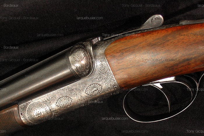 Fusil de chasse juxtaposé ancien. Bascule richement gravée de motifs floraux, canons brunis, crosse en bois et double détente.