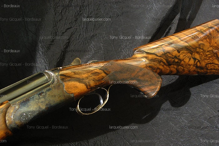 Fusil de chasse de luxe en bois précieux, crosse texturée, pontet doré et mécanisme détaillé. Watermarks Tony Gicquel - Bordeaux, larquebusier.com.