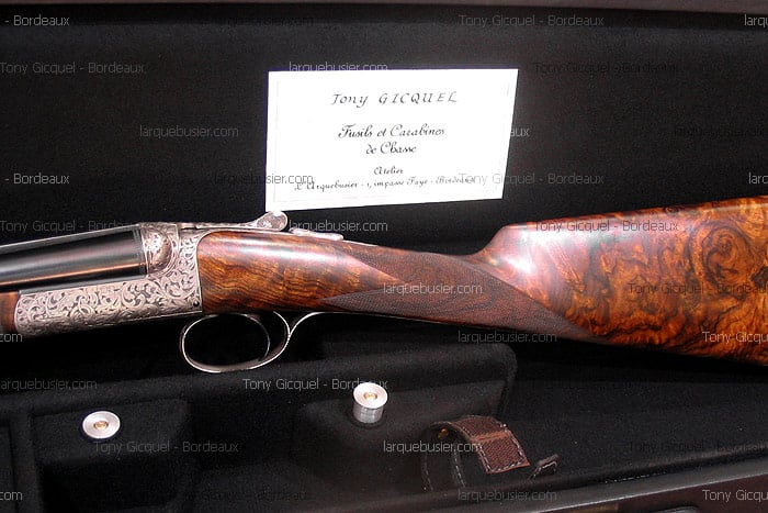 Fusil de chasse gravé de Tony Gicquel avec crosse en bois madré, présenté dans son étui. La carte indique 'Fusils et Carabines de Chasse'.