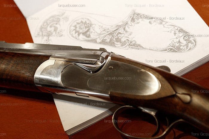 Fusil de chasse luxueux avec son récepteur poli, posé sur un dessin détaillé de gravure florale. Mentions : larquebusier.com, Tony Gicquel - Bordeaux.