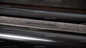 Gros plan d'une surface métallique sombre et brillante, avec une gravure en relief de 'Aland 53' sur une bande texturée.