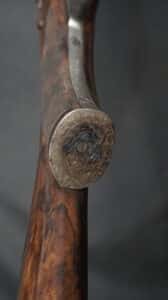 Poignée d'arme à feu en bois noble, ornée d'une plaque de couche métallique argentée finement gravée de volutes. Détail élégant.