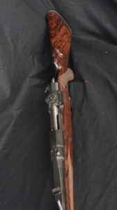 Carabine de chasse à verrou avec crosse en bois de noyer lustrée et veinée, et mécanismes métalliques sombres, vue de dessus.