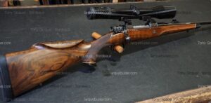 Carabine de chasse à verrou en bois précieux avec lunette de visée, posée sur une surface sombre. Mentions: Tony Gicquel - Bordeaux, larquebusier.com.