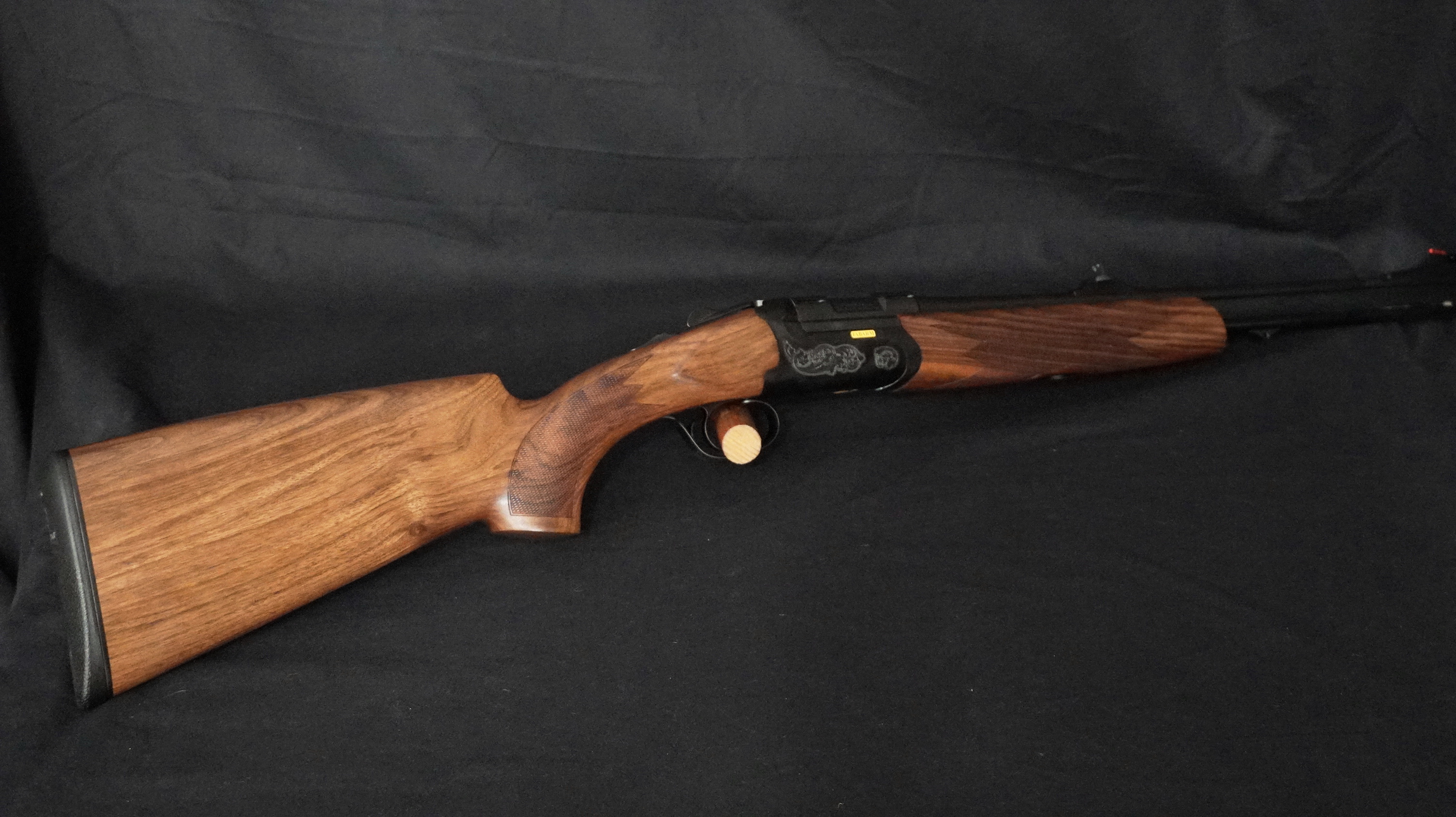 Carabine de chasse Sabatti en bois foncé, métal noir gravé et inscription dorée. Crosse texturée.