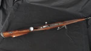 Carabine de chasse à verrou avec crosse en bois de noyer richement veiné et finition polie, posée sur fond noir.
