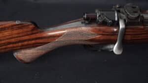 Crosse en bois de noyer veiné avec quadrillage fin d'une carabine de chasse. Levier de culasse et action en métal sombre visible.