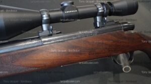 Carabine Winchester Modèle 70 avec lunette Leupold montée sur un boîtier de culasse en acier, crosse en bois foncé quadrillée.
