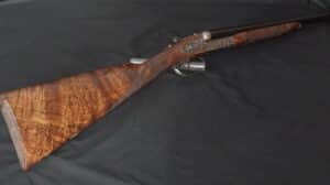 Fusil de chasse haut de gamme, crosse en bois de noyer ronceux aux motifs riches, gravures détaillées sur le récepteur.