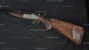 Fusil de chasse élégant, crosse en bois veiné et mécanisme finement gravé. Mentions "larquebusier.com" et "Tony Gicquel - Bordeaux".