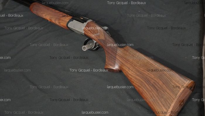 Fusil de chasse moderne sur fond sombre. Crosse et devant en bois veiné, boîtier de culasse gris métal. Marquages : Tony Gicquel - Bordeaux et larquebusier.com.