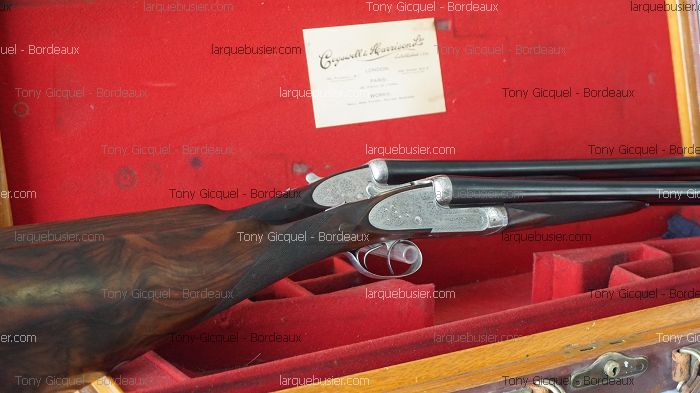 Fusil de chasse juxtaposé Cogswell & Harrison Ltd dans son étui rouge, crosse en bois veiné et platines gravées. Carte d'entreprise visible.