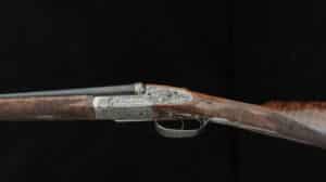 Fusil de chasse luxueux avec crosse en bois veiné et gravures détaillées sur le récepteur en métal argenté et doré.