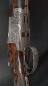 Close-up d'un fusil de chasse gravé. Le récepteur en métal argenté orné de volutes florales et une crosse en bois veiné brun.