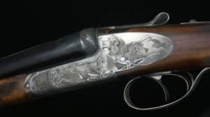 Fusil de chasse de luxe avec gravures artistiques de trois chiens et d'oiseaux sur le boîtier argenté. Crosse en bois foncé et incrustation de perle.