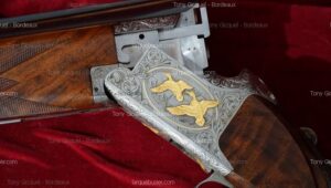 Fusil de chasse de luxe ouvert, crosse en bois, receveur argenté finement gravé avec deux canards dorés et motifs floraux.