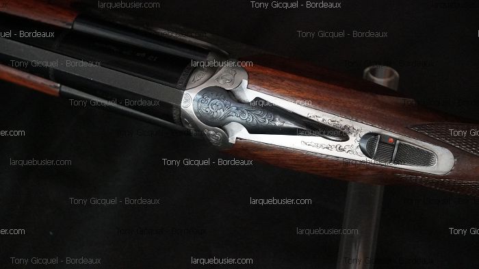 Gros plan sur un fusil de chasse à crosse bois sombre, avec une platine gravée de motifs floraux. Sûreté visible. Crédits Tony Gicquel - Bordeaux.