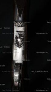 Gravure détaillée d'un fusil de chasse de luxe avec tête de cerf, rinceaux floraux et textes 'Tony Gicquel - Bordeaux', 'larquebusier.com'.
