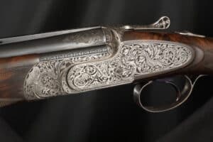 Détail d'un fusil de chasse orné, présentant des gravures complexes de dragons et de motifs floraux sur le boîtier de culasse argenté et le bois foncé.