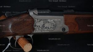 Fusil de chasse avec crosse en bois et culasse gravée de deux sangliers. Texte visible : Tony Gicquel - Bordeaux, larquebusier.com.