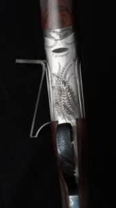 Récepteur de fusil de chasse T. Gicquel gravé de plumes détaillées, en acier poli avec crosse en bois foncé.