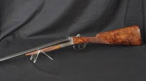Fusil de chasse juxtaposé de collection, canon noir, boîtier gravé, crosse en ronce de noyer sur fond noir.