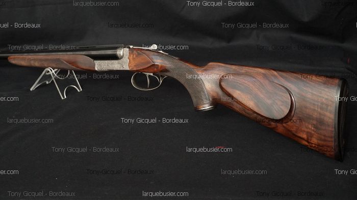 Fusil de chasse juxtaposé en bois sombre veiné et acier gravé, sur support. Marques Tony Gicquel - Bordeaux et larquebusier.com.