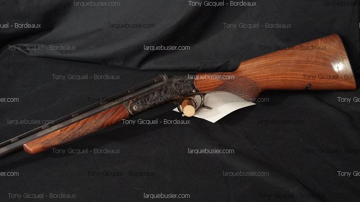 Fusil de chasse juxtaposé, crosse bois, boîtier gravé, sur fond noir. Vendu par Tony Gicquel - Bordeaux via larquebusier.com.