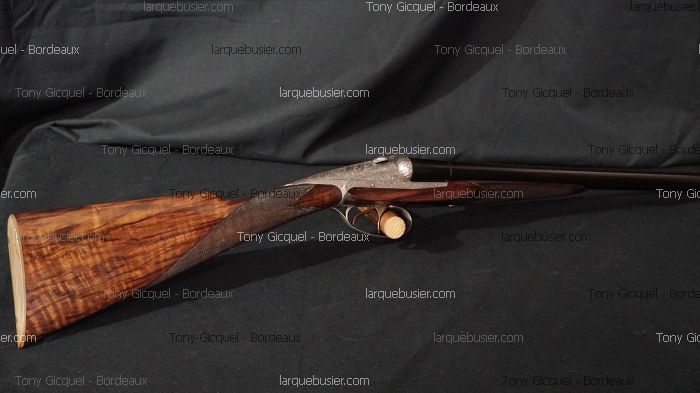 Fusil de chasse juxtaposé Tony Gicquel Bordeaux, crosse en noyer figuré et mécanisme gravé, sur fond sombre. larquebusier.com