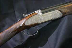 Fusil de chasse superposé, détail du boîtier de culasse gravé avec motifs floraux et de la crosse en bois finement quadrillé.