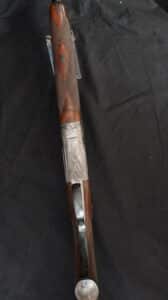 Fusil de chasse T. Grequel, crosse bois quadrillée, mécanisme métal gravé plumes. Luxueux et orné sur fond noir.