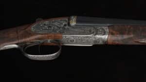 Détail d'un fusil de chasse de luxe. Crosse en bois veiné, boîtier de culasse en métal gravé de motifs floraux ornés et accents dorés.