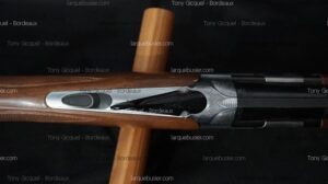 Détail du récepteur gravé d'un fusil de chasse, avec levier de déverrouillage argenté et crosse en bois. Tony Gicquel - Bordeaux.