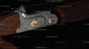 Détail du fusil de chasse Rizzini avec gravures florales complexes et incrustation dorée d'une perdrix en vol sur la bascule en bois.