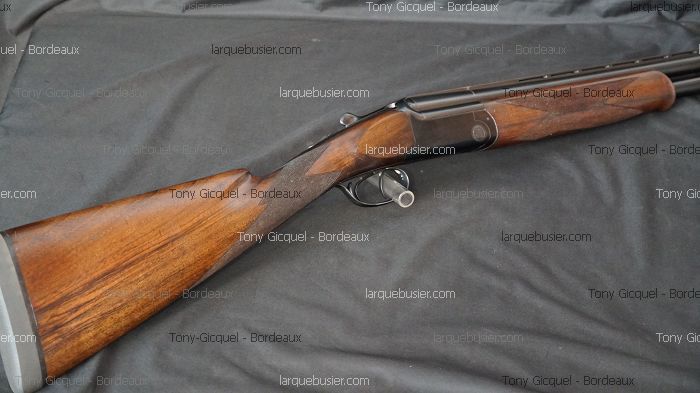 Fusil de chasse superposé, crosse et devant bois, canons noirs. Textes: "Tony Gicquel - Bordeaux", "larquebusier.com".