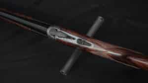 Fusil de chasse superposé avec crosse en bois marbré. Gros plan du boîtier de culasse en métal gravé et du sélecteur de tir rouge.