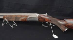 Fusil de chasse superposé, crosse et devant en bois figuré foncé, canon et bascule en métal poli. Repose sur un support transparent. Étiquette "No333".