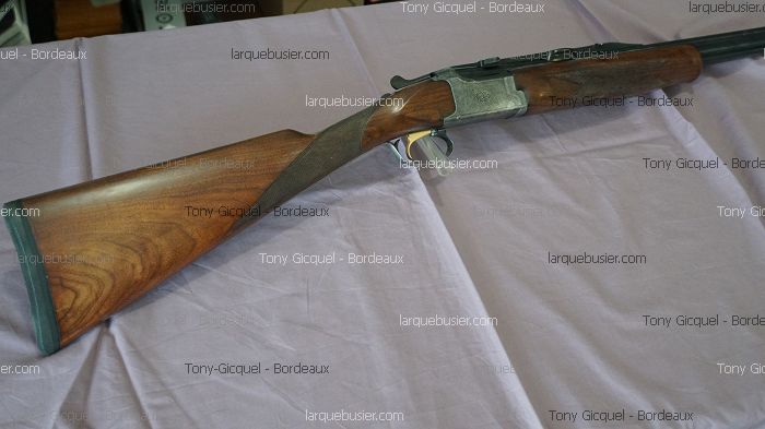 Fusil de chasse superposé avec crosse en bois et mécanisme argenté sur tissu. Textes 'Tony Gicquel - Bordeaux' et 'larquebusier.com'.