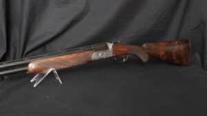 Fusil de chasse superposé "BORDEAUX" avec canon noir, crosse et devant en bois veiné, bascule gravée argentée sur fond noir.
