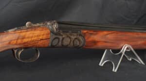Fusil de chasse juxtaposé ancien. Bois veiné, canon bleui, platines gravées de motifs floraux et trois médaillons en relief. Sur support.