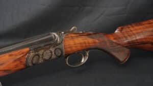 Fusil de chasse de luxe. Crosse et devant en bois figuré. Culasse en métal richement gravé. Levier de pouce moleté. Texte sur canon: "...rquel."