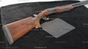 Fusil de chasse ou sport à canons superposés, crosse en bois et plaque de couche noire, posé sur un tissu foncé. Texte : Tony Gicquel - Bordeaux.
