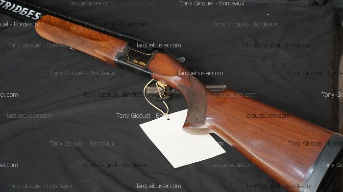 Fusil de chasse superposé en bois lustré, avec inscriptions 'Trap Ultra' sur la culasse et 'CARTRIDGES' sur le canon. Une étiquette vierge pend.